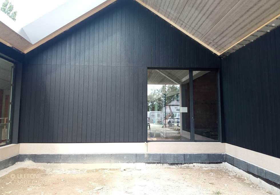Donkere verticale gevelbekleding met een grote raamopening.